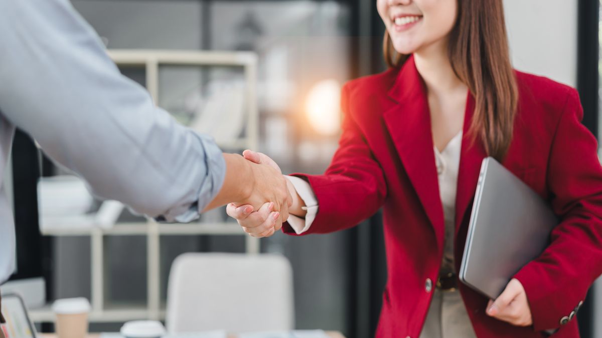 Businesswoman,In,Red,Blazer,Smiling,And,Shaking,Hands,With,Colleague